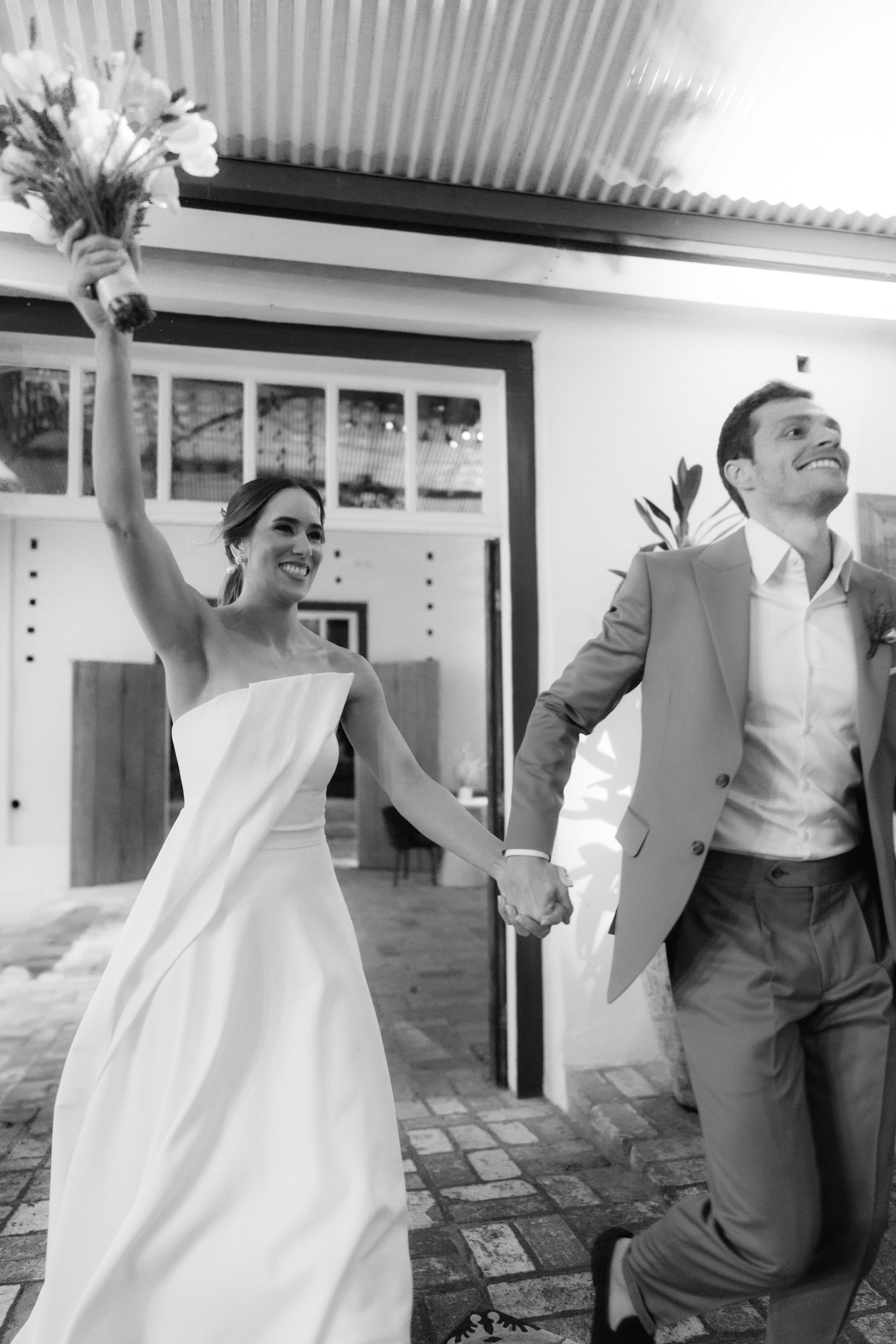 Joyful wedding couple celebrating with raised arms in black and white.