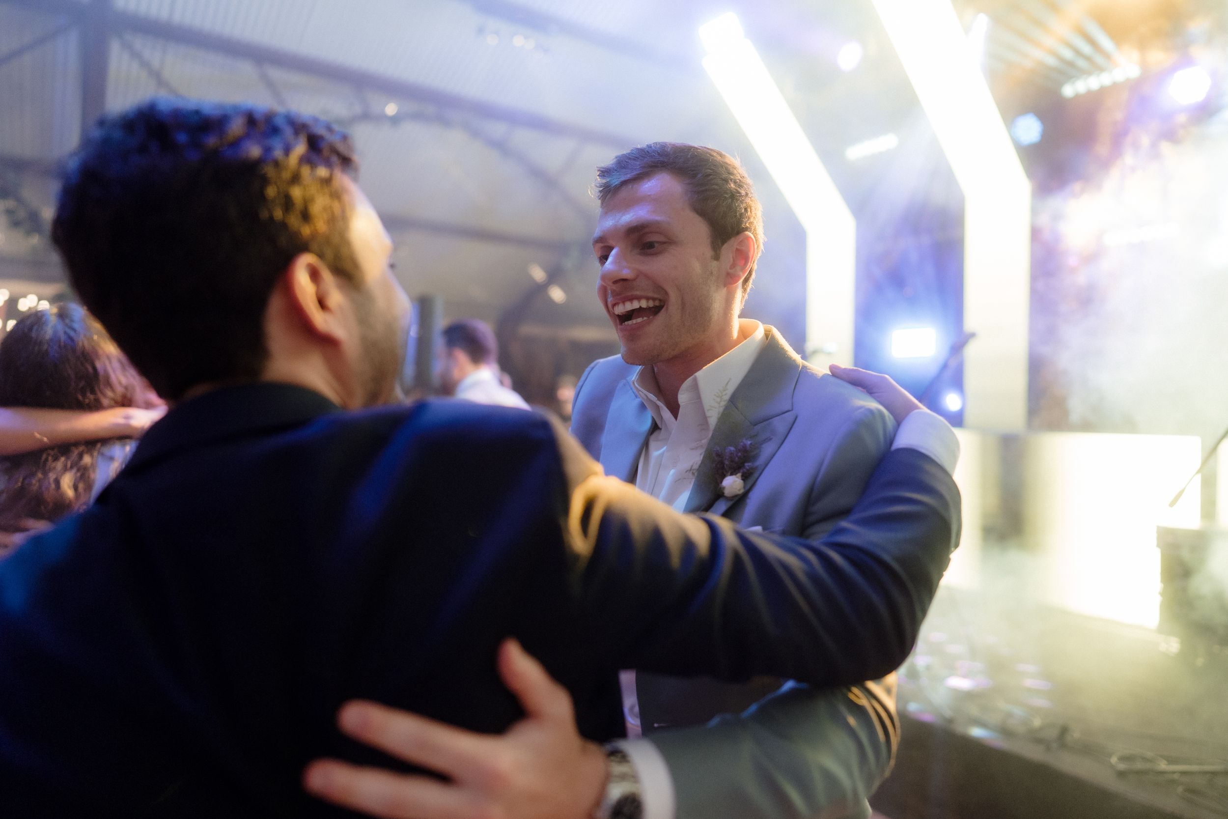 Two people laughing and embracing at a party with blue lighting.