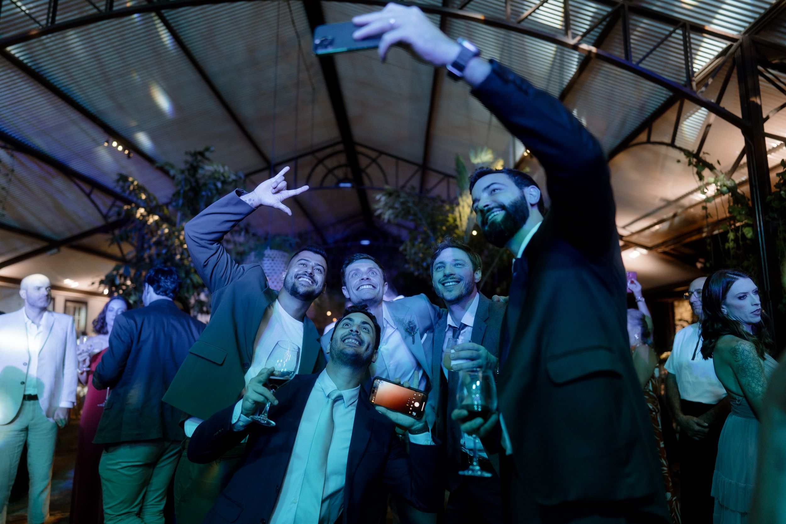 Group of party guests cheering with drinks under colorful lighting.