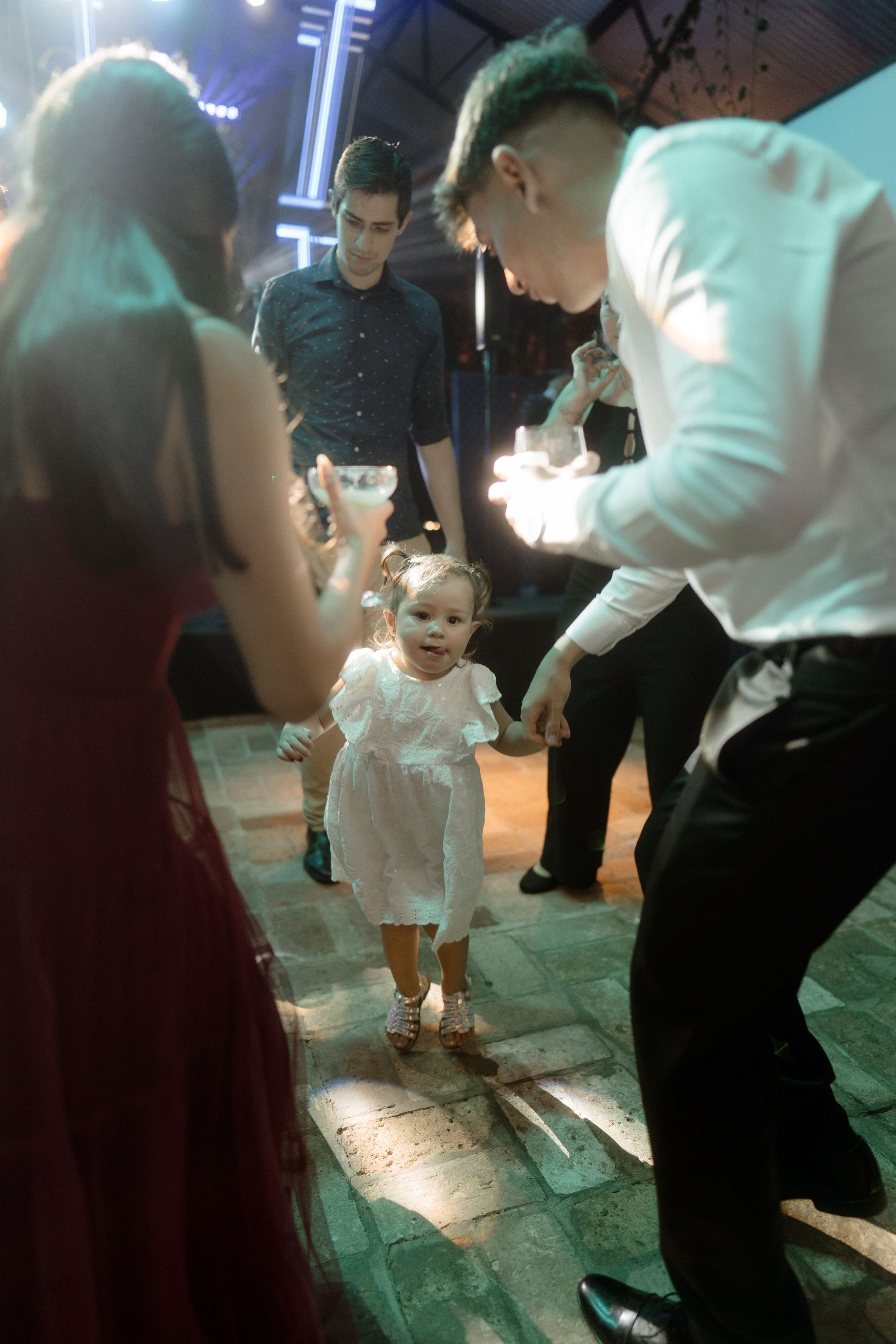 Small child in white dress dancing on an illuminated floor at a reception venue.