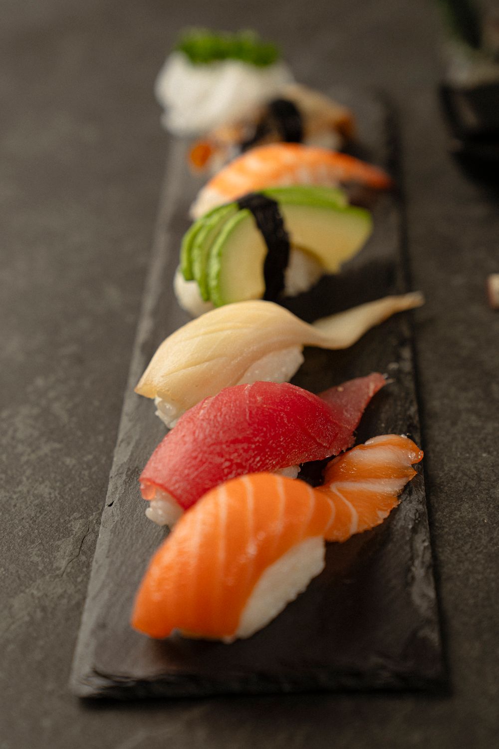 Assorted nigiri sushi featuring tuna, salmon, and white fish arranged on a black slate platter.