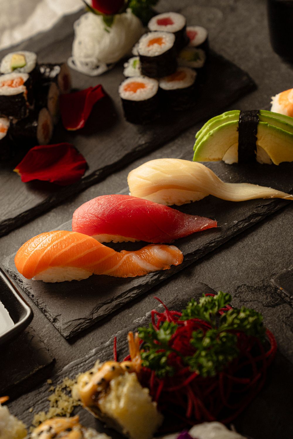 Fresh nigiri sushi and maki rolls beautifully presented on dark slate with garnishes.