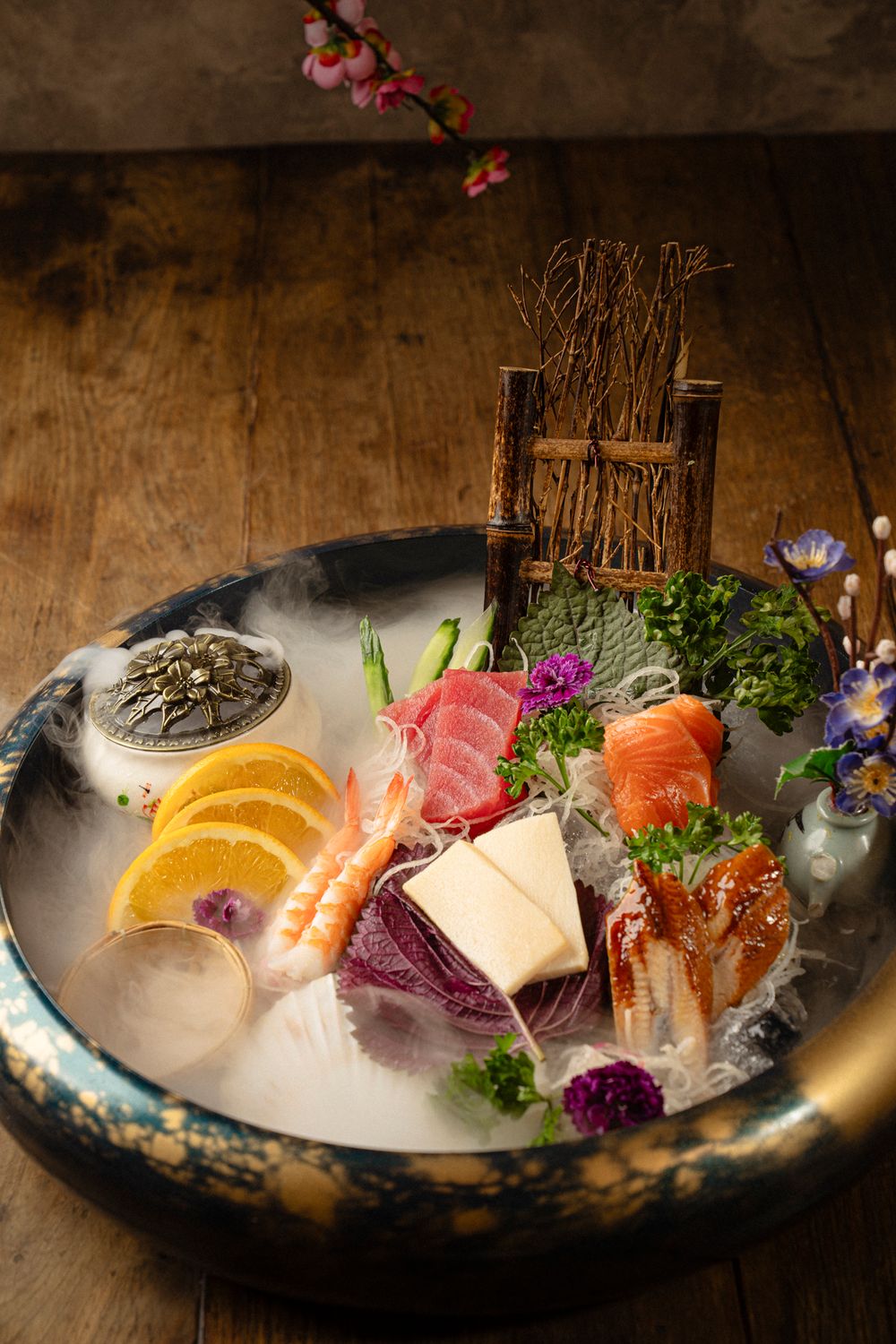 Elegant sashimi platter with fresh fish, orange slices and decorative flowers served on ice.