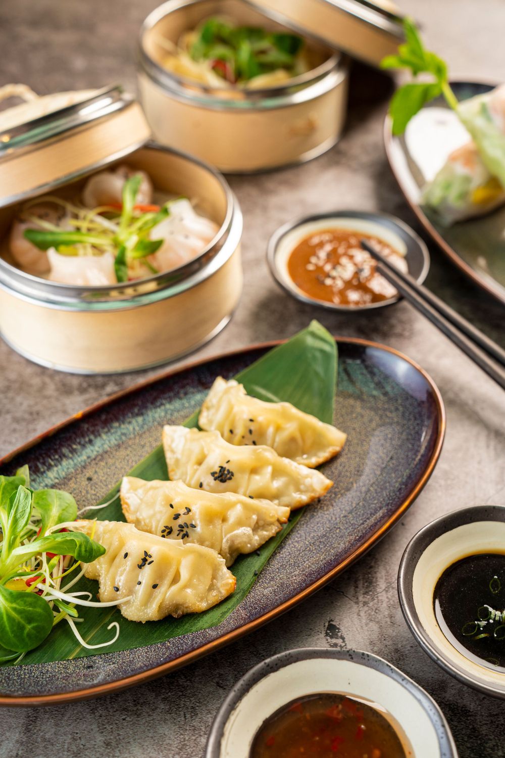 Steamed dumplings served on a blue ceramic plate with dipping sauces and garnished with fresh microgreens.