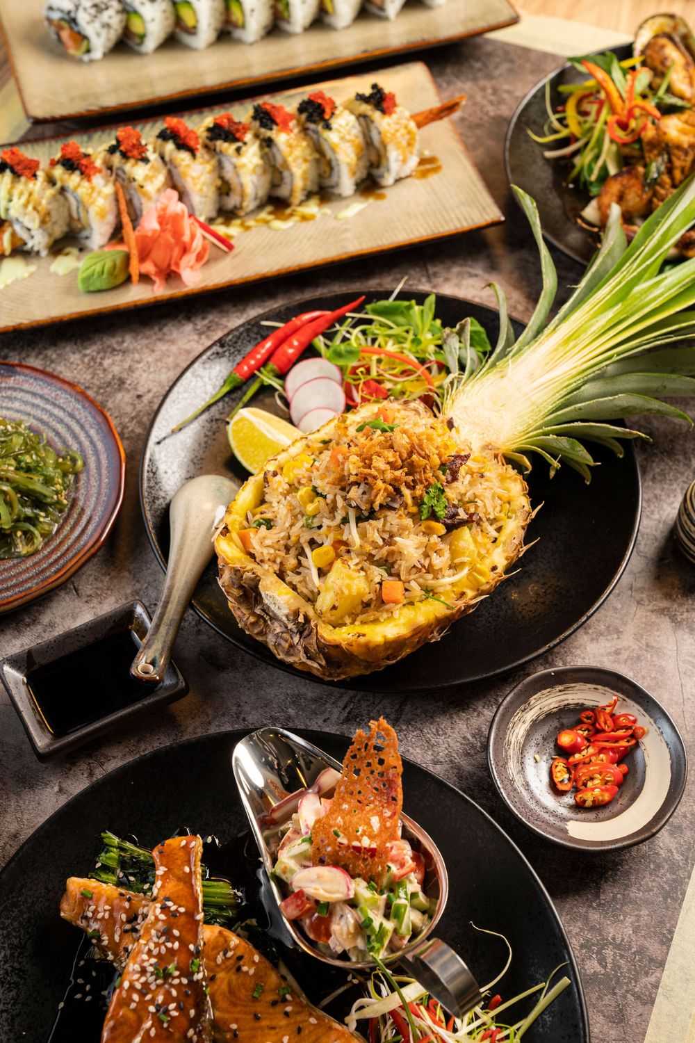 Elaborate Asian fusion spread featuring pineapple fried rice, sushi rolls and appetizers.