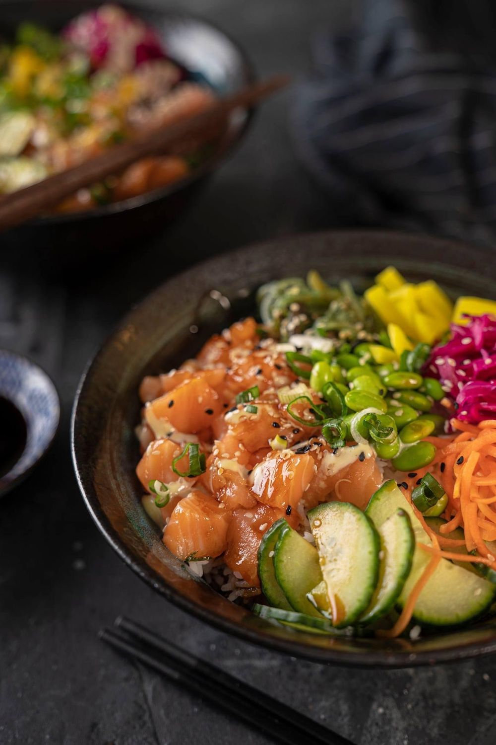 Fresh salmon poke bowl with cucumbers, carrots and colorful vegetables on dark background.