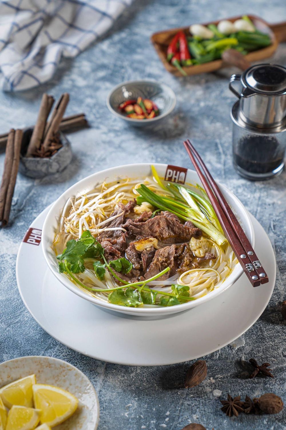 Vietnamese pho noodle soup with beef, herbs and lime wedges served with chopsticks.
