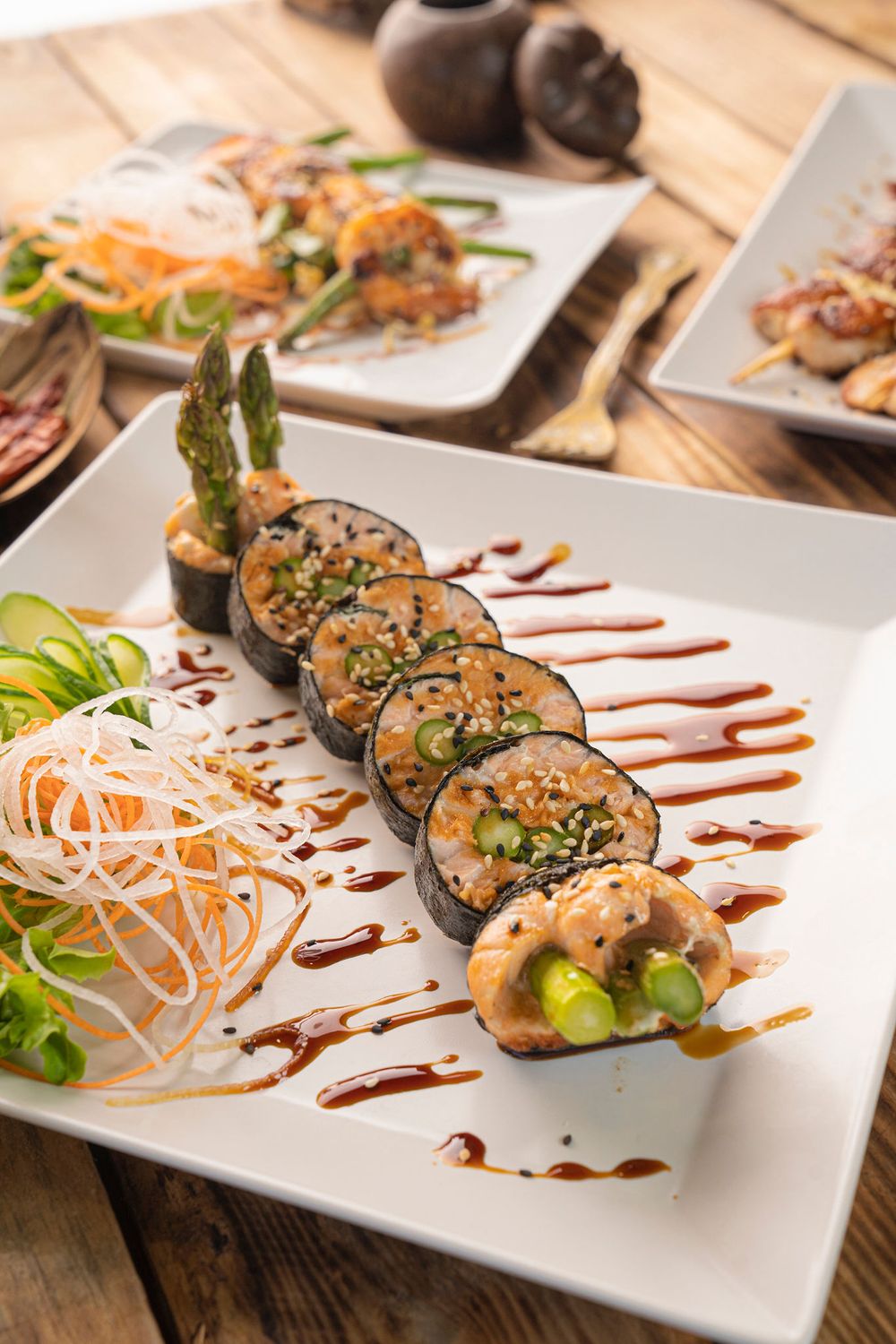 Beautifully plated vegetable sushi rolls with sauce drizzle and noodle garnish on white plate.