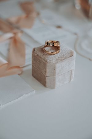 Gold wedding rings rest elegantly on a velvet beige ring box against a white surface with soft peach accents.