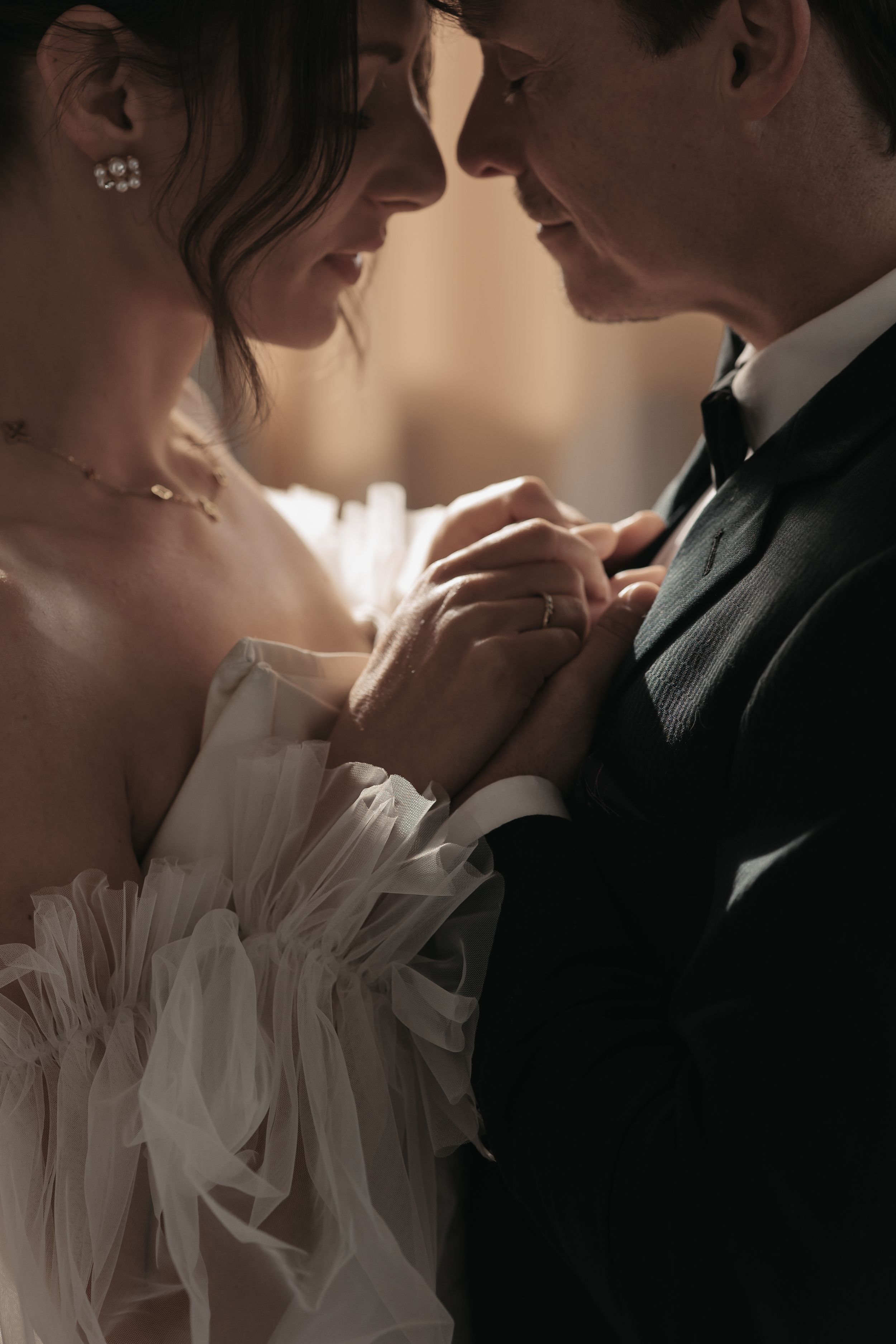 Close-up romantic shot of a couple on their wedding day with clasped hands and white tulle gown details.