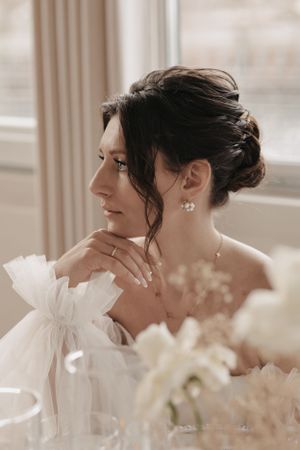 An elegant bride in a white gown at a wedding reception with a soft focus and delicate pearl earrings.