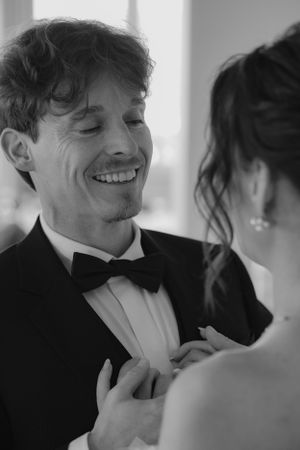 Black and white photo of intimate wedding moment as couple shares joyful laughter during formal celebration.