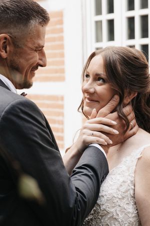 Groom tenderly cups bride's face as she gazes up at him lovingly during outdoor wedding portrait session.
