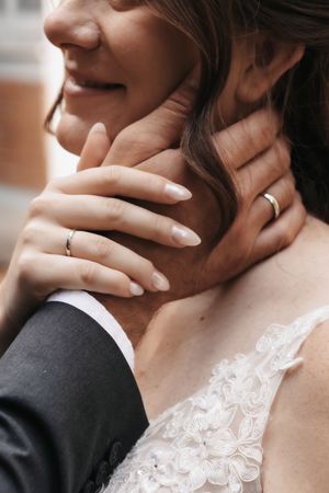 Close-up of bride and groom hands with wedding rings, groom tenderly holding brides neck in lace wedding dress.