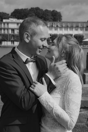 Black and white photo of a smiling couple in wedding attire embracing outdoors, groom in suit and bride in lace dress.