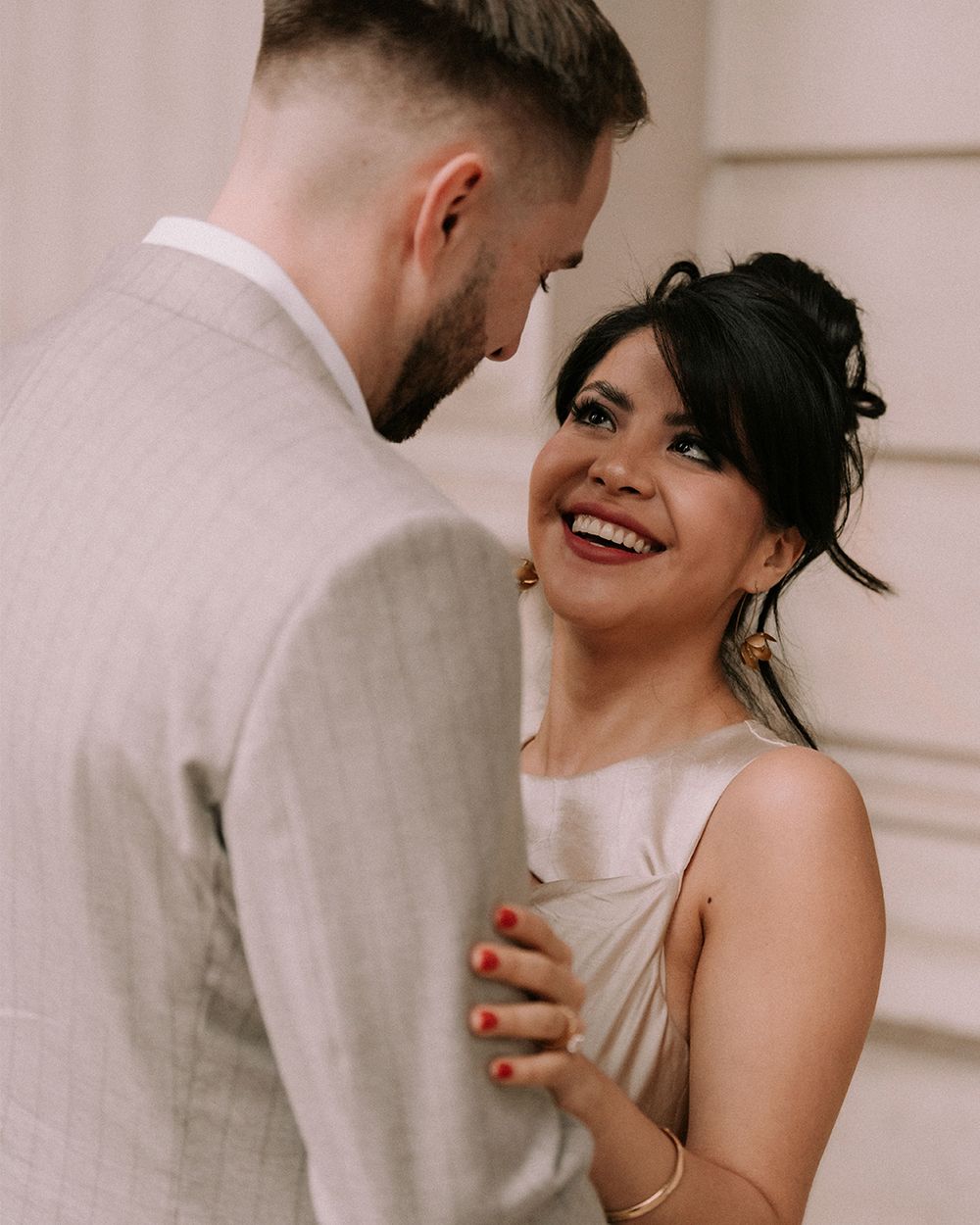 A smiling bride in a silver dress gazes at her groom in a light gray suit during an elegant wedding ceremony.