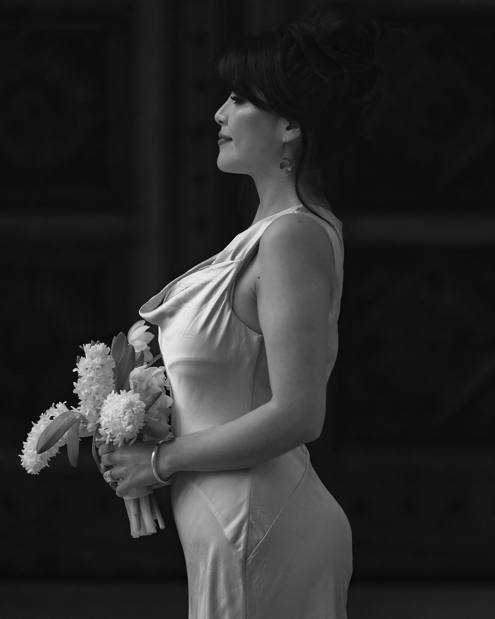 Black and white photo of a bride in a sleeveless gown holding a bouquet, gazing upward with an elegant updo.