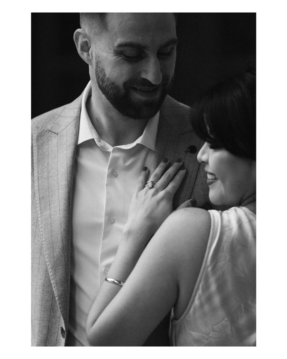 Black and white photo of a couple sharing a tender moment, woman placing hand on mans chest showing engagement ring.