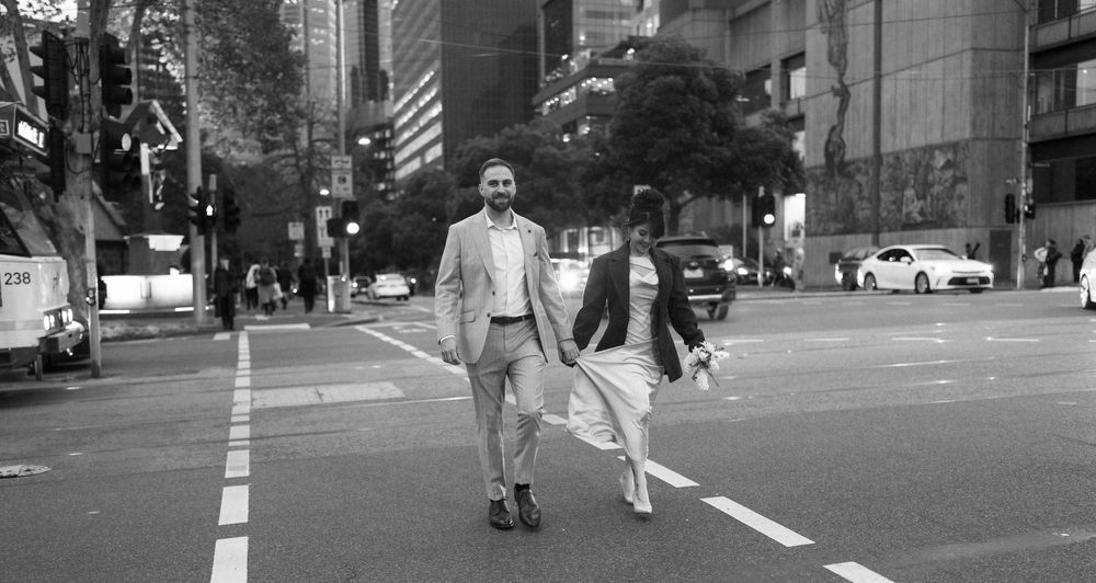 Couple walking hand in hand across a city street in black and white wedding attire.
