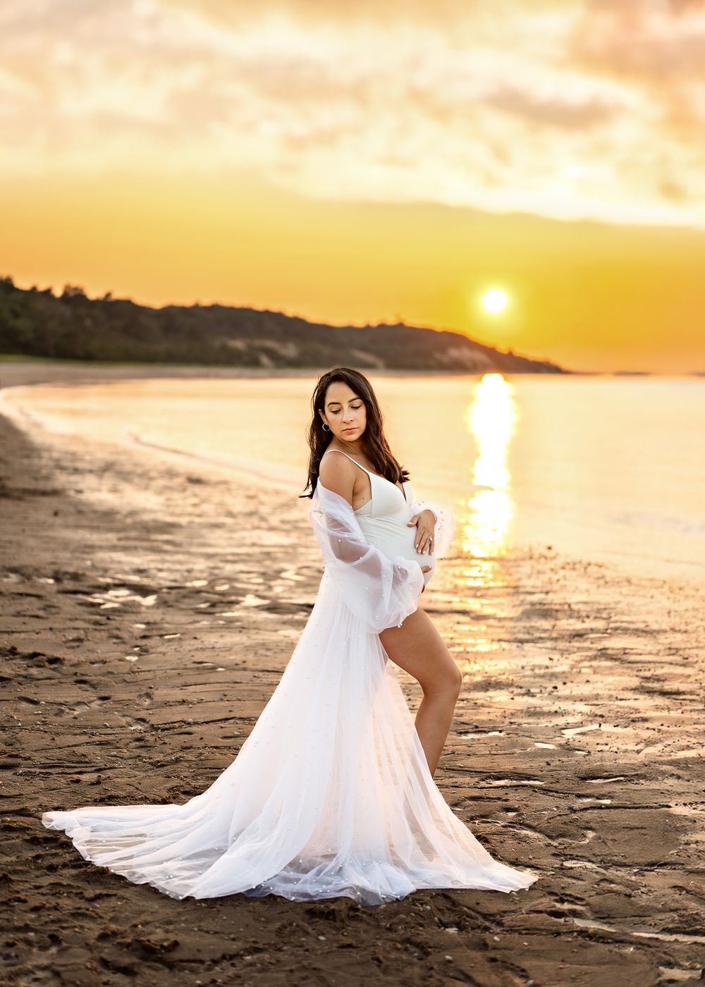 A flowing white dress catches the golden light during a sunset beach photoshoot along the shoreline.