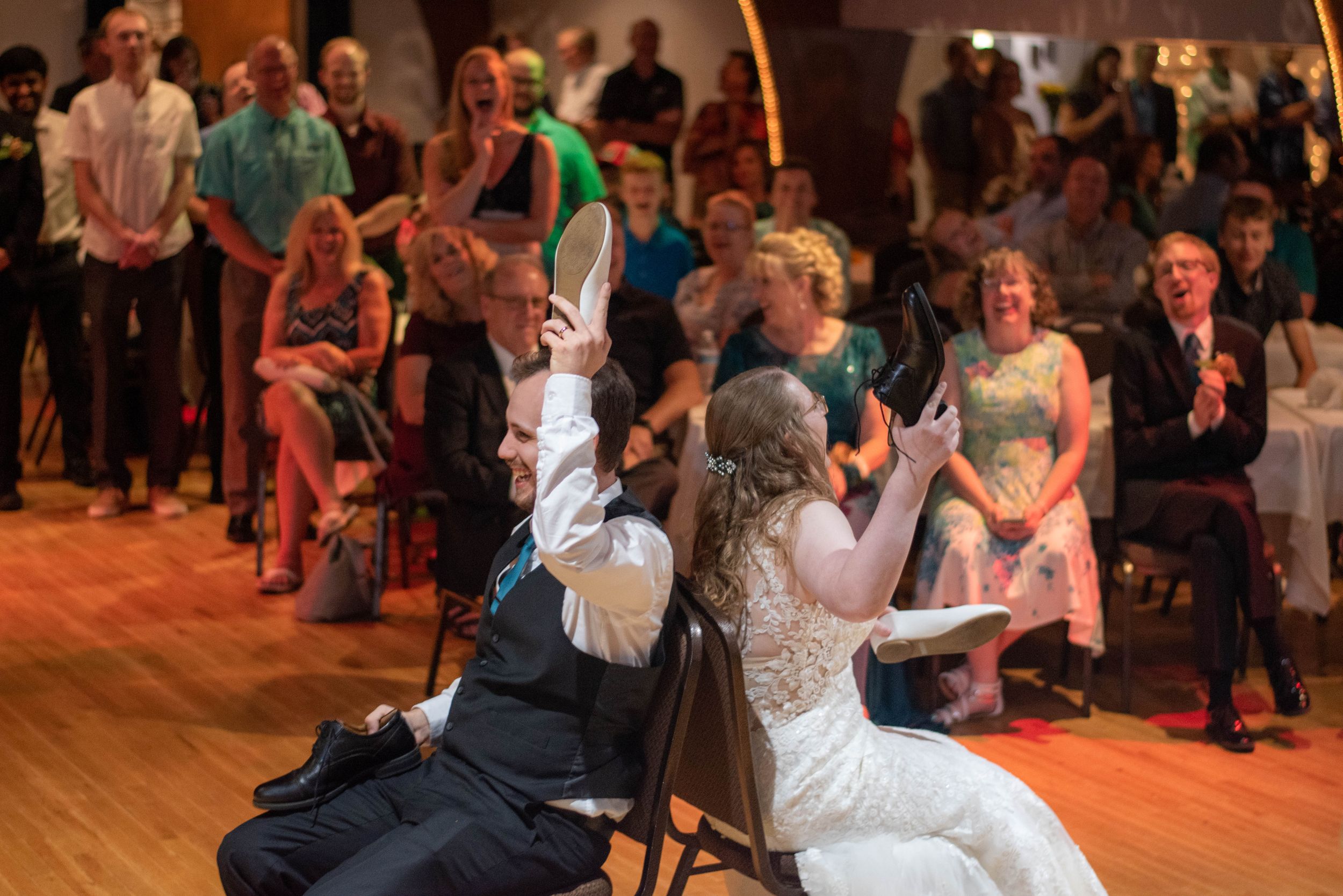 A bride and groom dance with wedding guests during their reception on a wooden dance floor.