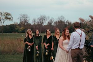 Wedding party in emerald green dresses stands in autumn field.