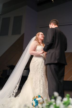 A bride and groom share their first kiss during a church wedding ceremony with a cross in the background.