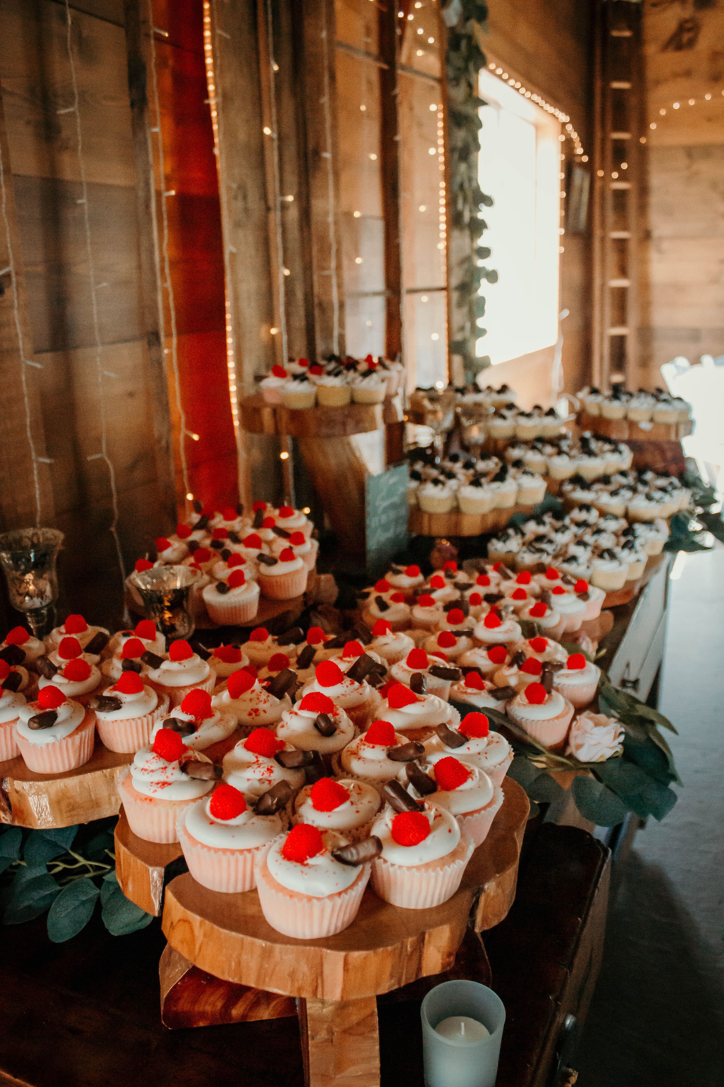 White cupcakes with red cherry toppings displayed on wooden slices at a wedding reception.
