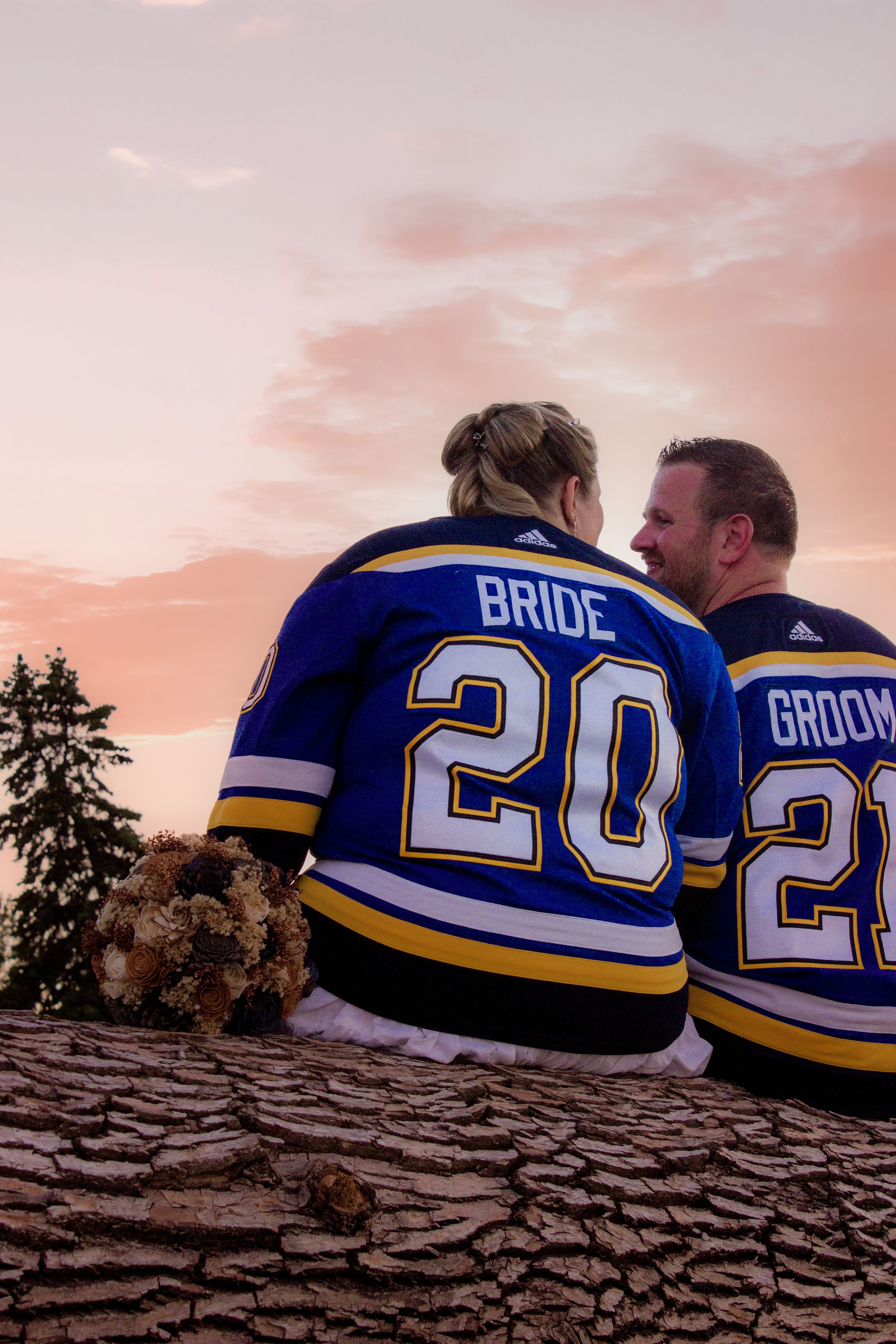 A couple wearing matching hockey jerseys with Bride and Groom numbers sits together at sunset.