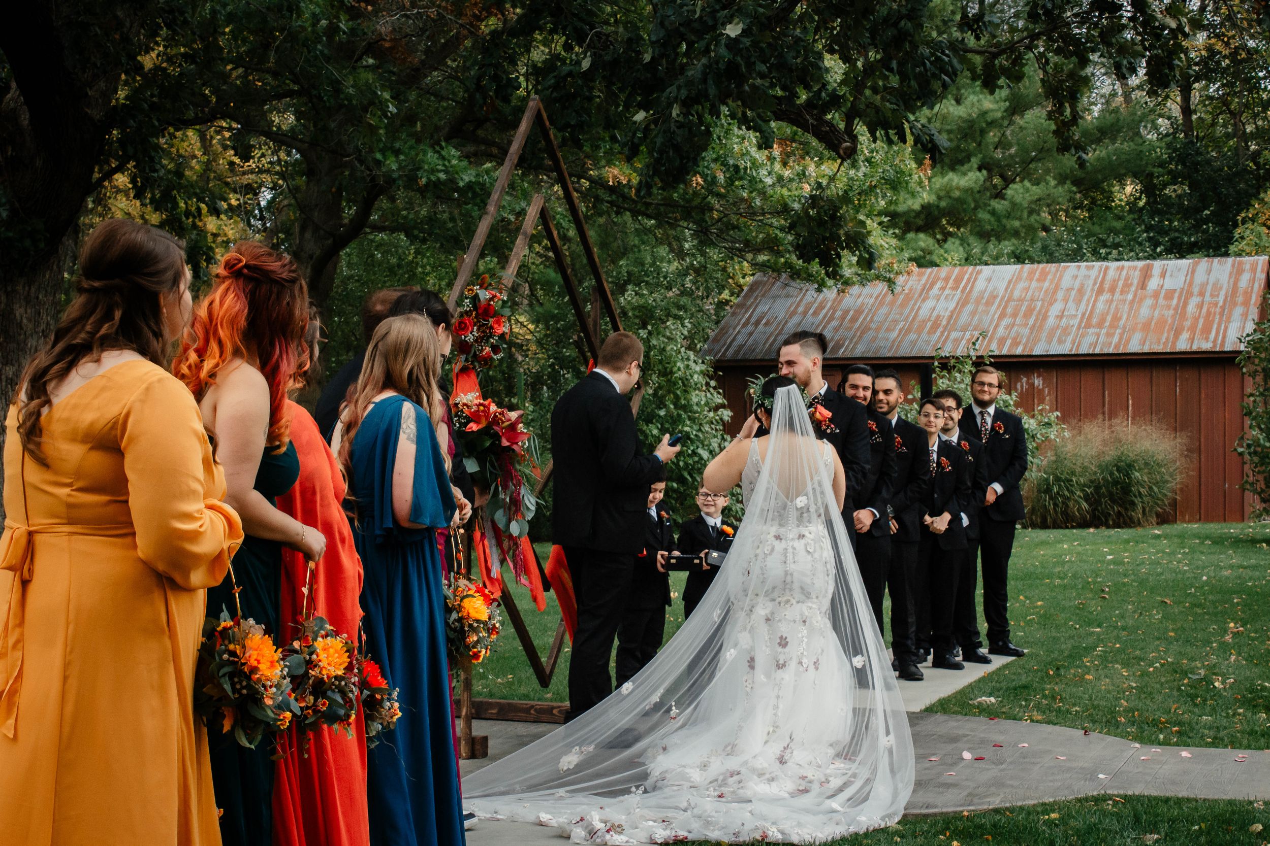 Outdoor wedding ceremony under wooden arch with colorfully dressed wedding party.
