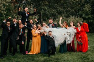 Fun wedding party photo with colorful dresses and suits on garden lawn.