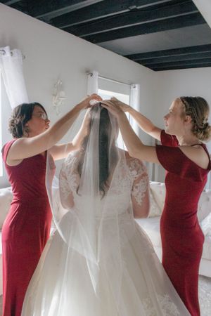 People in red dresses help hang a white lace wedding gown in preparation for the ceremony.