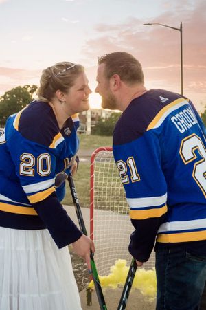 A couple in matching hockey jerseys shares a romantic moment while holding hockey sticks at sunset.
