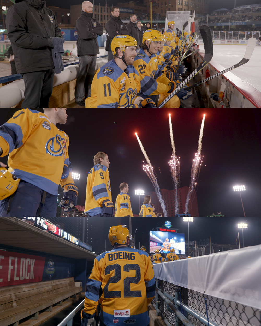 Hockey players in yellow jerseys share a moment at the boards while fireworks light up the stadium during a game.