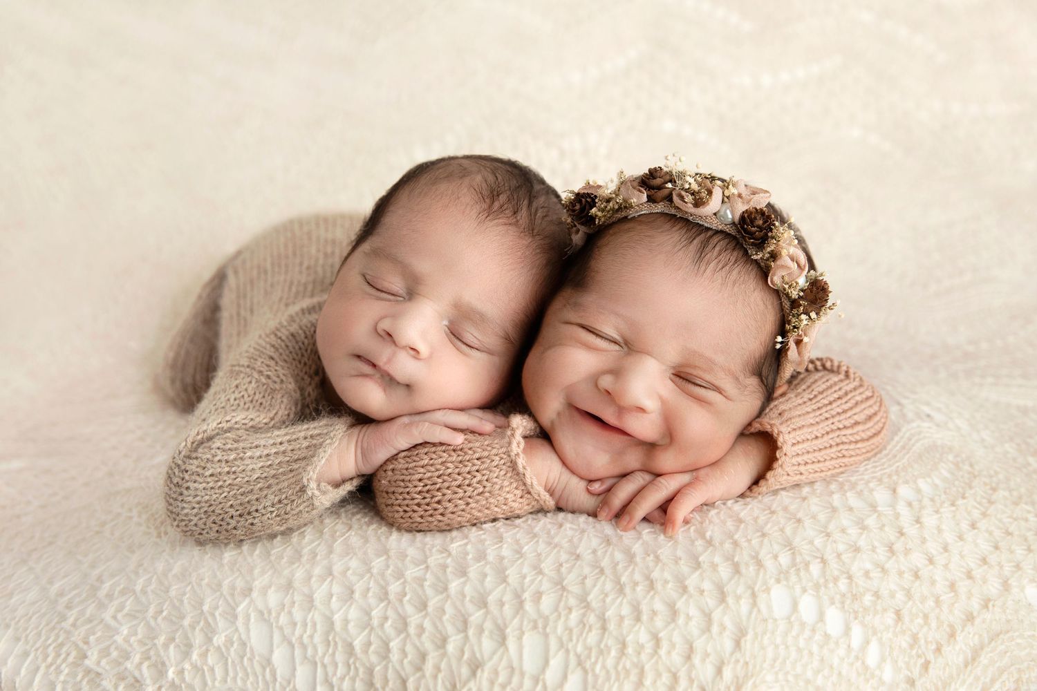 Two sleeping infants wearing knit outfits on cream textured backdrop.