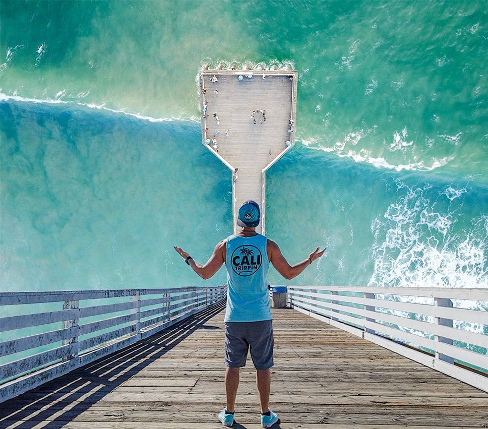 Inverted aerial photo of a man on a San Diego ocean pier wearing a CaliTrippin tank top, overlooking turquoise water.