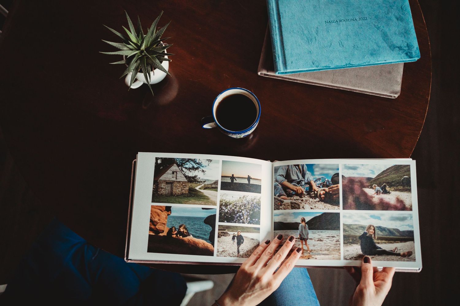 Hands flip through a photo album on a wooden table with coffee and books nearby, featuring vacation and travel memories.