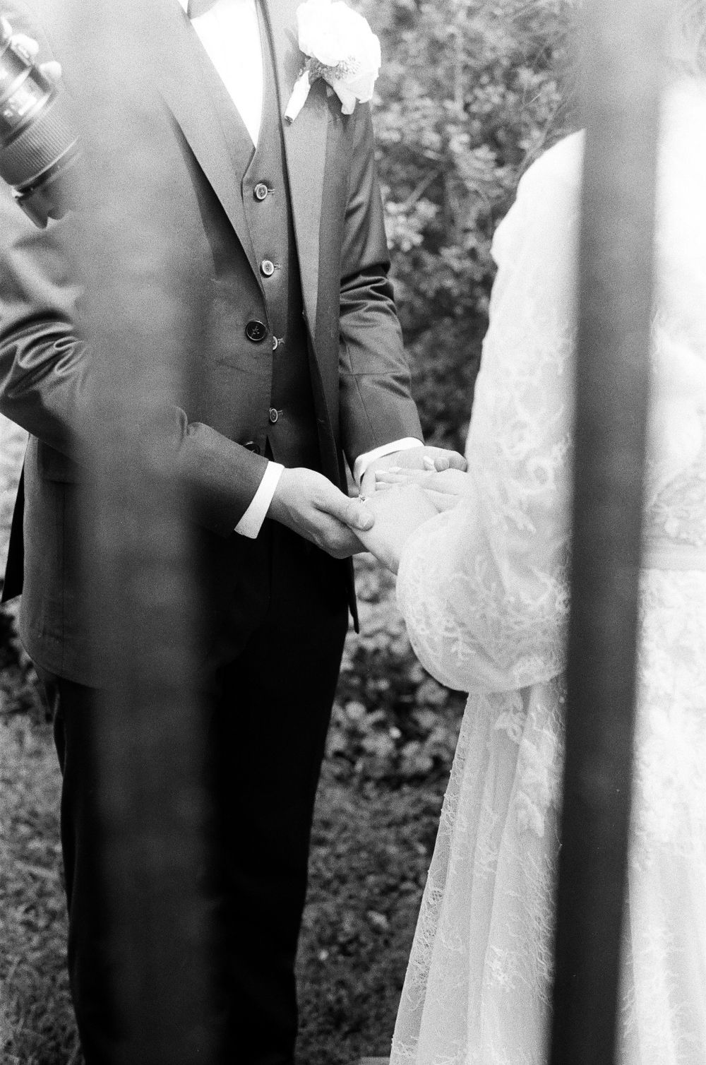 Black and white close-up of bride and groom holding hands during outdoor wedding ceremony.