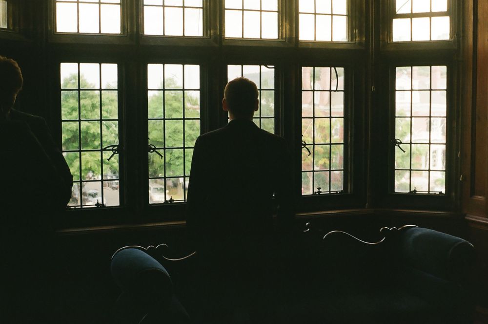 Silhouettes of two people sitting by large windows overlooking lush green trees.