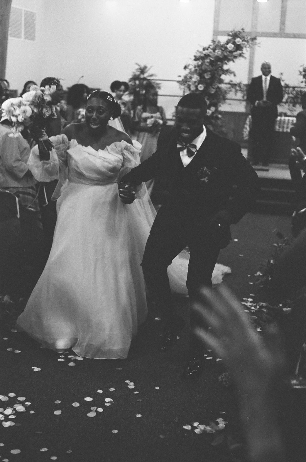 Joyful newlyweds dancing down the aisle after ceremony in black and white photo.