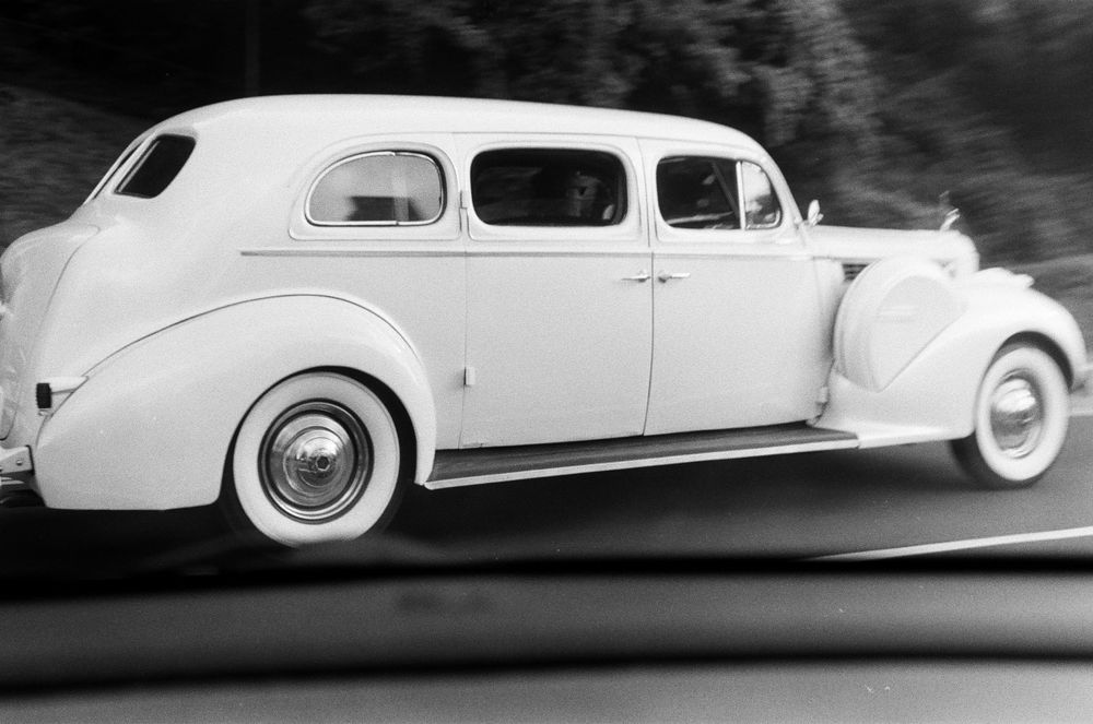 Vintage white classic car driving on a road, captured in black and white photography.