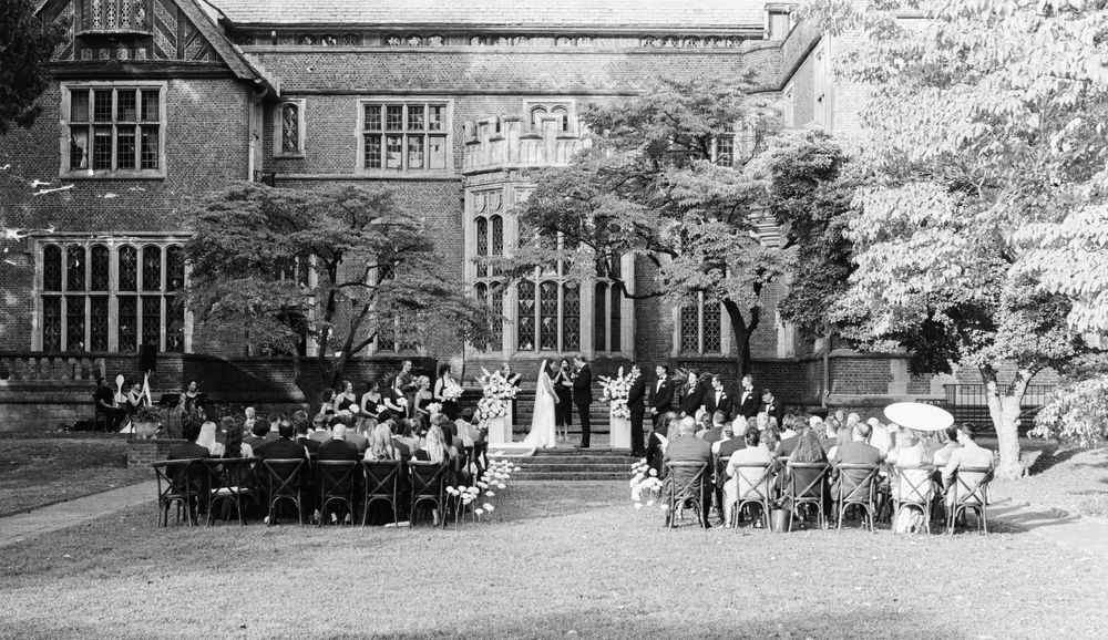 Elegant outdoor wedding reception on a lawn beside a grand historic manor building.