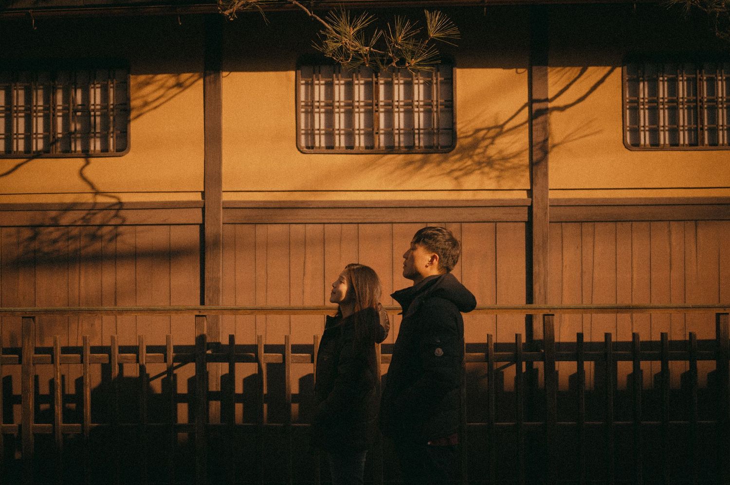 Two people walking past a warmly lit traditional Japanese building at night.