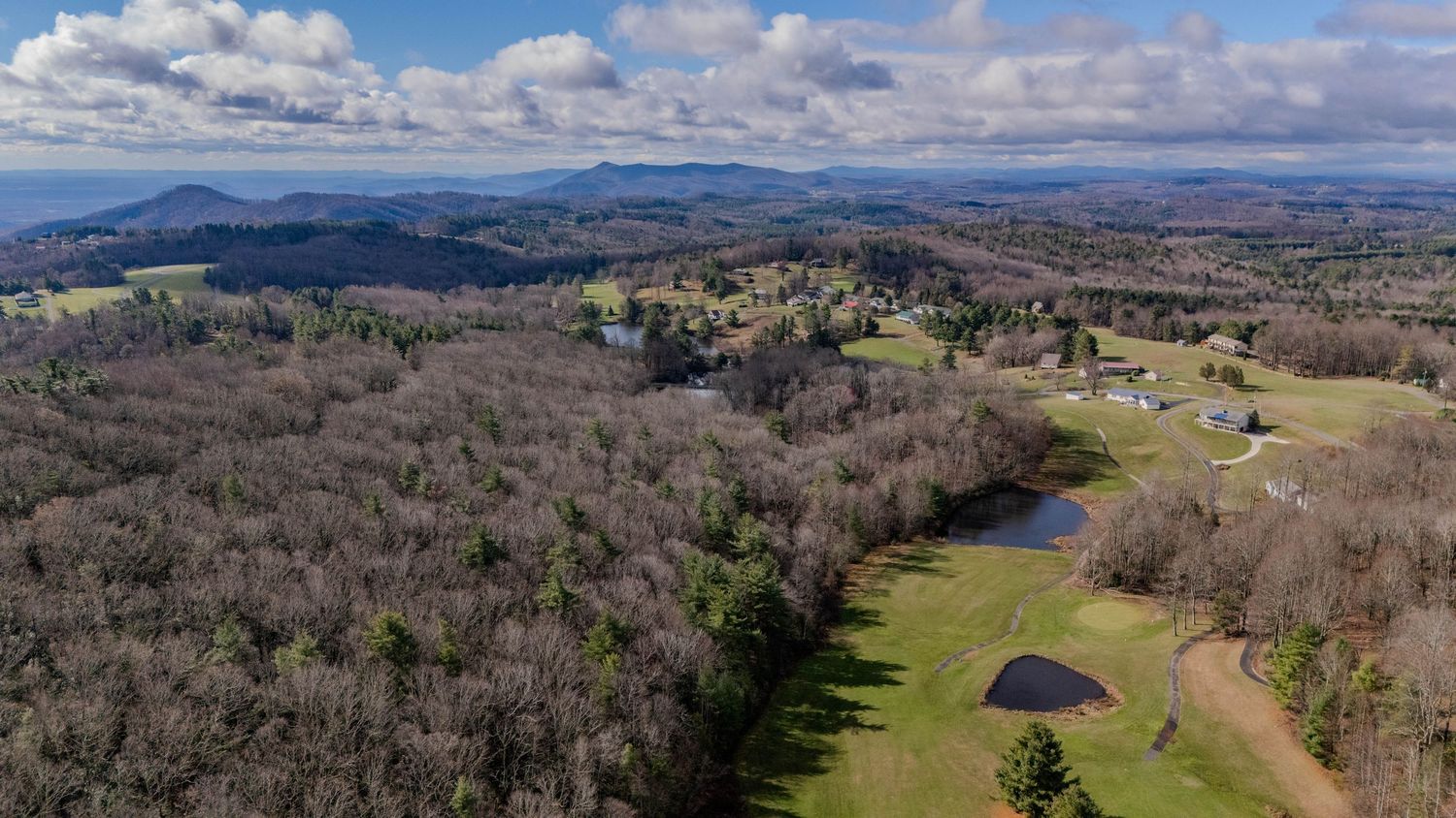 Drone shot of mountainous terrain with winding roads and scattered buildings among bare winter trees.