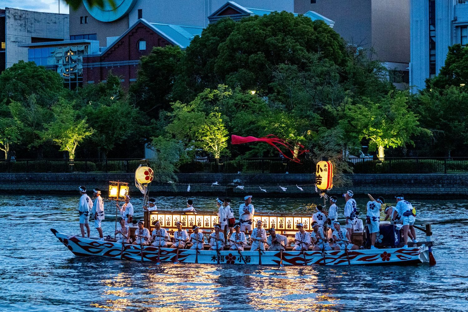 Illuminated festival boats gather on a river at night with glowing lanterns.