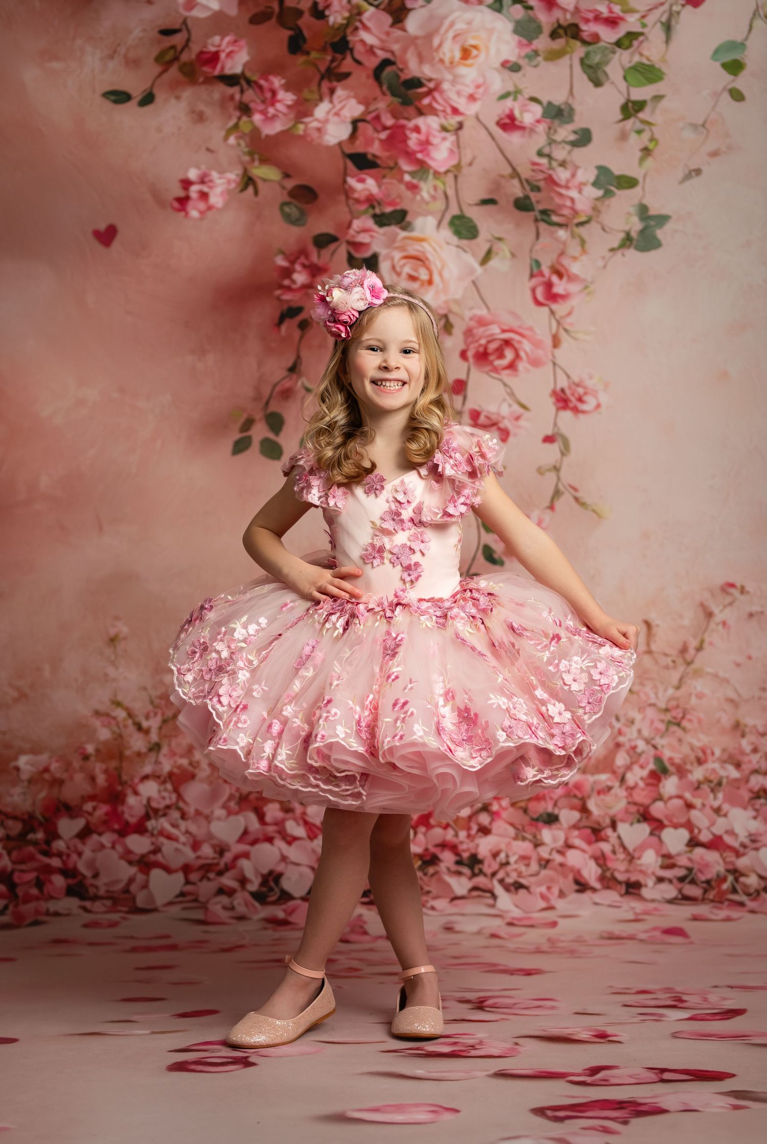 A stunning coral and pink ballgown with ruffled layers photographed against a soft peach floral backdrop.