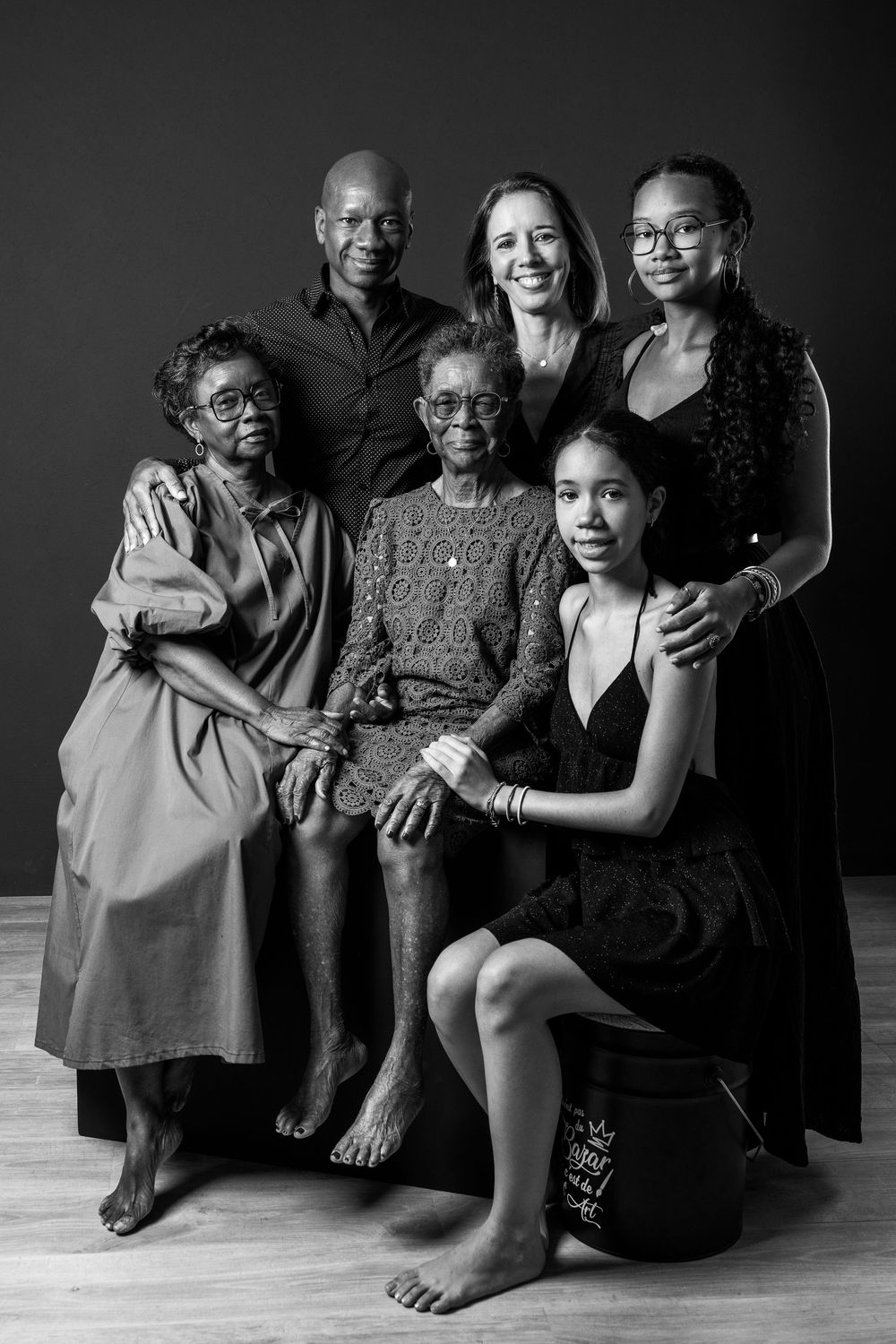 A black and white portrait shows a multi-generational family group of six people arranged in an intimate composition.