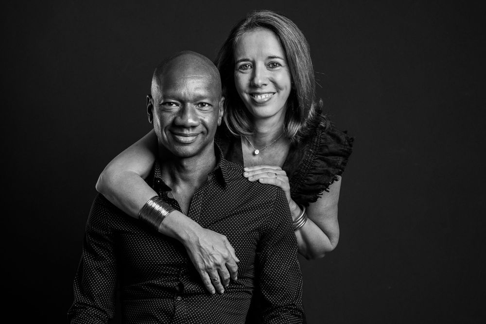 A black and white studio portrait of a couple smiling warmly against a dark background.