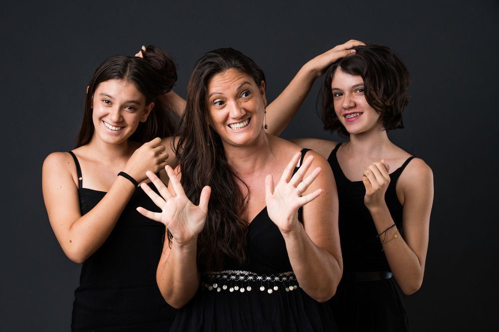 Three people in black outfits pose playfully against dark background with expressive hand gestures.