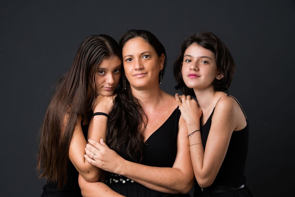 Three people wearing black tops pose together against dark background in intimate portrait.